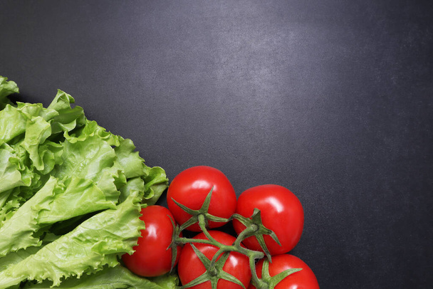 Green lettuce leaves red ripe tomatoes on a branch. Vegetables on a black textured background. - Fotoğraf, Görsel
