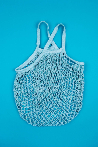 Top view of turquoise empty reusable string mesh eco bag for shopping on blue background. Zero waste and plastic free concept. Sustainable lifestyle. - Photo, image