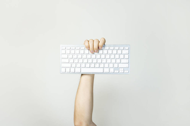Чоловіча рука тримає клавіатуру на світлому ізольованому фоні. Технологічна концепція, ремонт комп'ютерів, програміст, кодувальник, ІТ. банер
. - Фото, зображення