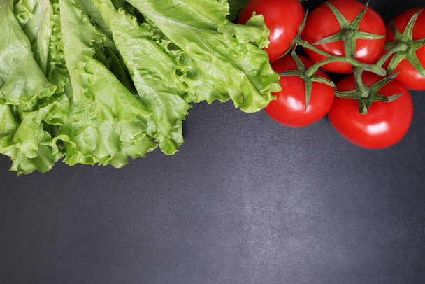 Green lettuce leaves red ripe tomatoes on a branch. Vegetables on a black textured background. - Foto, immagini