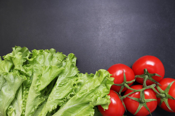 Green lettuce leaves red ripe tomatoes on a branch. Vegetables on a black textured background. - 写真・画像