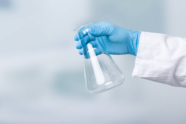 mano en guantes sostiene un matraz vacío delante de un fondo de laboratorio
 - Foto, imagen