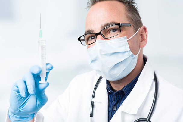 médico con aguja inyectable y estetoscopio frente a una sala de la clínica en segundo plano
 - Foto, imagen