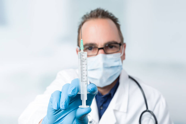 médico con aguja inyectable y estetoscopio frente a una sala de la clínica en segundo plano
 - Foto, imagen
