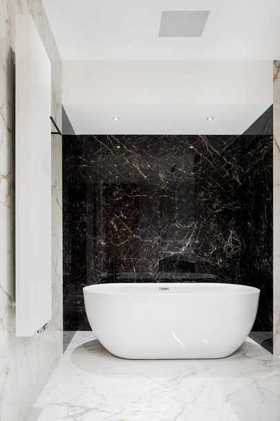 Luxury big oval bathtub in bathroom with black and white marble tiles on walls and floor - Фото, изображение