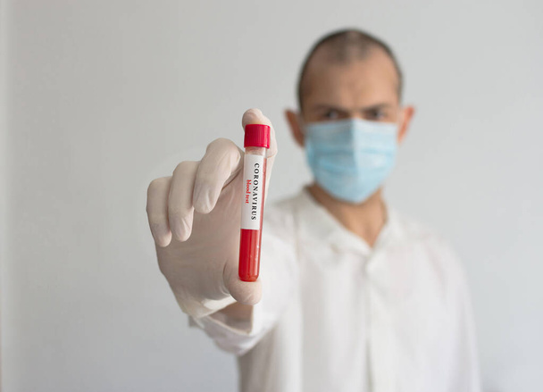Arzt mit medizinischer Gesichtsmaske und Handschuhen, in der Hand ein Bluttestergebnis für den Ausbruch des Coronavirus COVID-19. Coronavirus Bluttest konzeptionelles Foto. - Foto, Bild