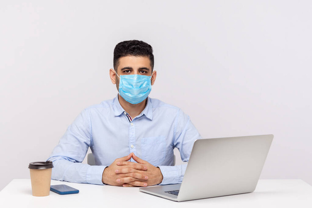 Male employee wearing hygienic mask and looking at camera, sitting in office using protect filter against contagious disease coronavirus, 2019-nCoV, flu epidemic. indoor studio shot, white background - Photo, Image
