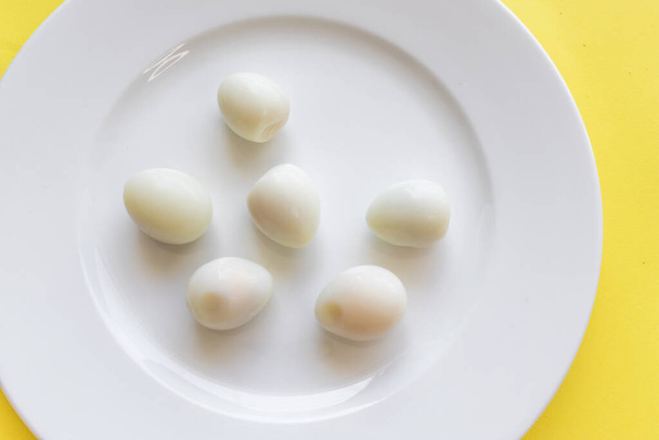 Set of peeled organic small boiled quail eggs on white plate on yellow background. Top view, copy space. Healthy protein fresh natural food. Natural gourmet meal. Little bird eggs. Close up photo. - Foto, Imagem