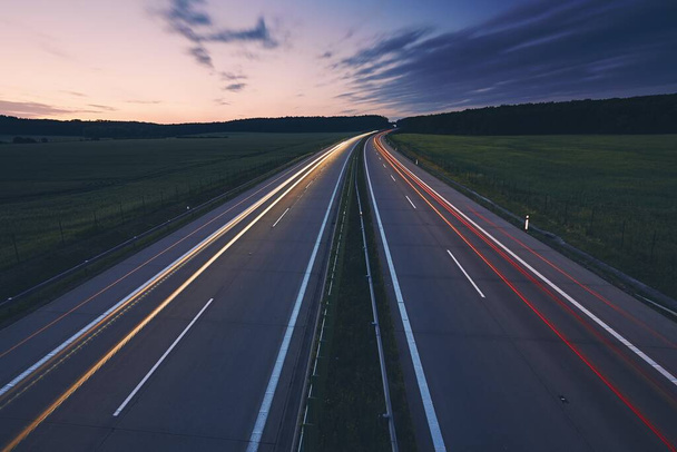 Sentiers lumineux des voitures. La circulation sur l'autoroute au milieu des champs à l'aube beuatiful
. - Photo, image