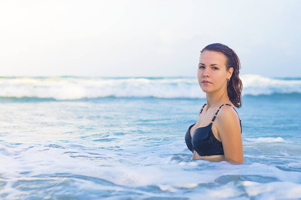Sexy beautiful serious girl in bikini standing in clear blue water with waves, posing, looking at camera. Young confident woman swimming in tropical sea, enjoying summer vacation, holidays, travel - Fotografie, Obrázek