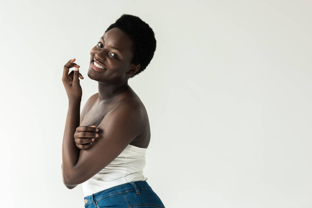 cheerful african american girl in jeans and white top isolated on grey - Foto, Imagem