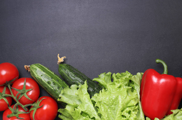 Green lettuce, red ripe tomatoes on a branch, fresh cucumbers and red bell peppers paprika. Vegetables on a black textured background. - Foto, immagini