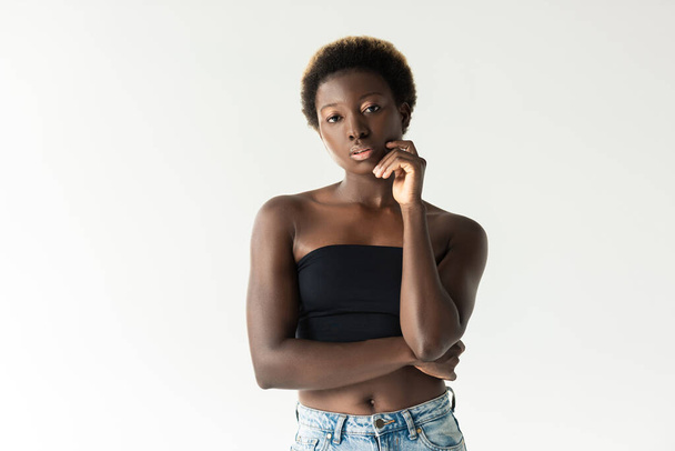 thoughtful african american girl in jeans and black top isolated on grey - 写真・画像