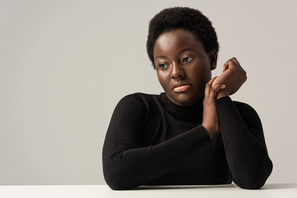 pensive african american woman in black turtleneck sitting at table isolated on grey - Foto, immagini