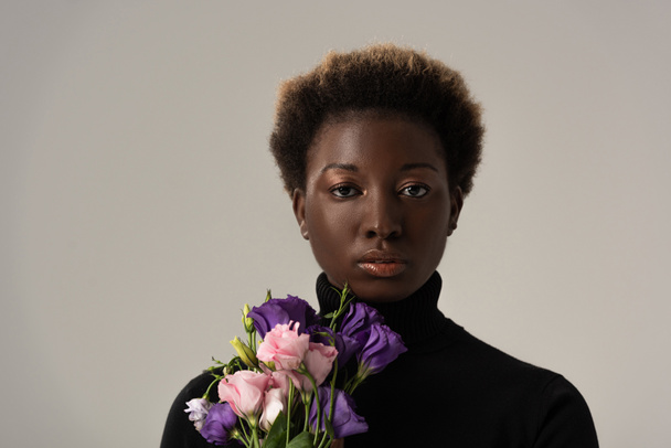 attractive african american woman in black turtleneck holding eustoma flowers isolated on grey - Foto, afbeelding