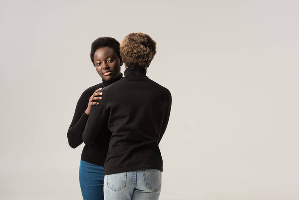 gelukkig afrikaanse amerikaanse vrouwen in zwart turtlenecks knuffelen geïsoleerd op grijs - Foto, afbeelding