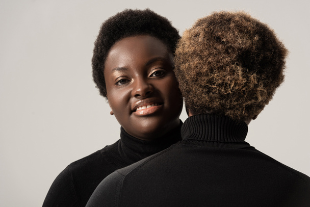 sorridenti ragazze africane americane in dolcevita neri che si abbracciano isolate sul grigio
 - Foto, immagini