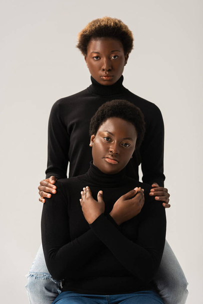 afro-amerikai barátnők fekete garbó ölelés elszigetelt szürke - Fotó, kép