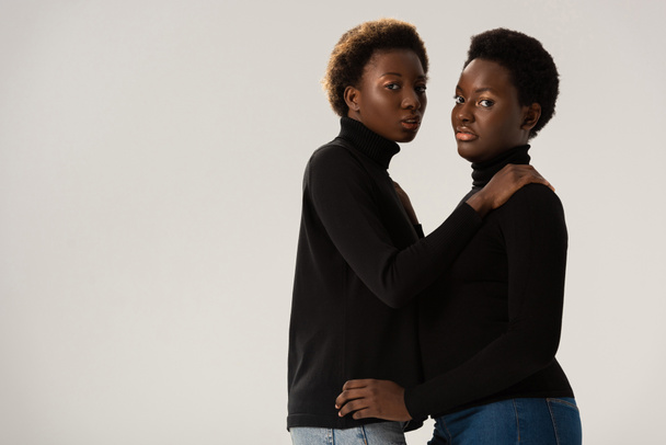 african american girlfriends in black turtlenecks hugging isolated on grey - Foto, imagen