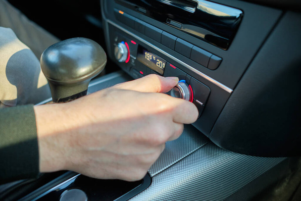 Ένας άνθρωπος σε ένα σύγχρονο αυτοκίνητο. Το χέρι αλλάζει το επίπεδο θέρμανσης του καθίσματος. Κλείσε.. - Φωτογραφία, εικόνα