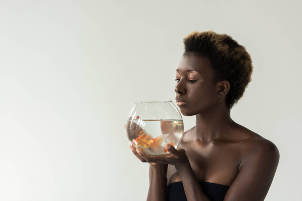 attractive african american girl holding aquarium with fish isolated on grey - Foto, afbeelding