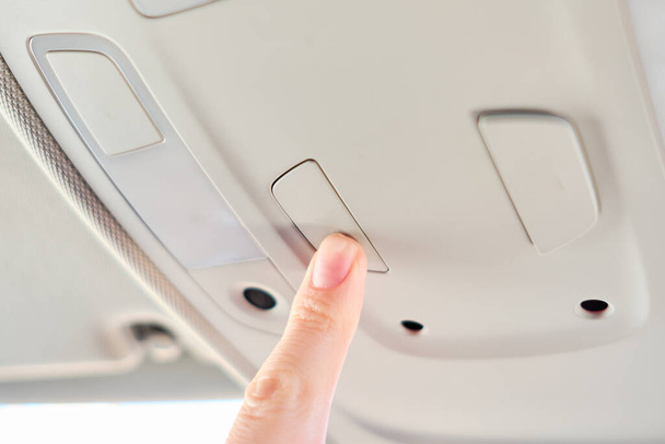 Egy férfi egy modern autóban. Kézzel nyomja meg a gombot a lámpával a panelen. Közelről.. - Fotó, kép