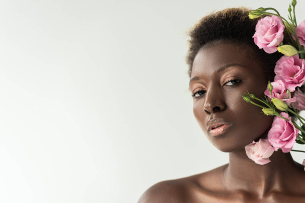 Pembe Eustoma çiçekleri olan çıplak Afro-Amerikalı kadın, gri renkte izole edilmiş. - Fotoğraf, Görsel