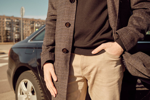 A man in a coat holds his hands in jeans near the car. Close up. - Foto, afbeelding