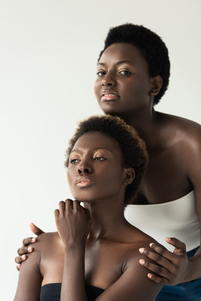 bedachtzame Afrikaanse Amerikaanse vriendinnen in toppen geïsoleerd op grijs  - Foto, afbeelding