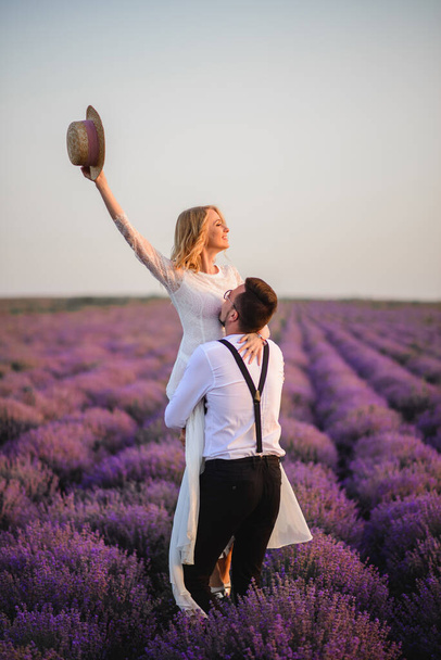 Happy groom holding his bride in his arms in blooming lavender field at sunset - Fotografie, Obrázek
