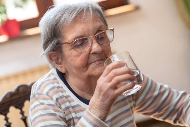 Donna anziana che tiene un bicchiere d'acqua a casa
 - Foto, immagini