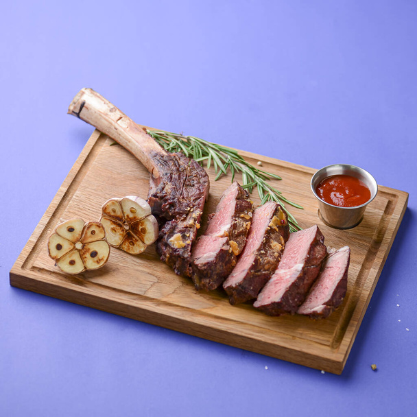 Grillé en tranches Barbecue moyen rare Steak sur os aux épices servi sur une planche de bois rustique sur fond bleu
. - Photo, image