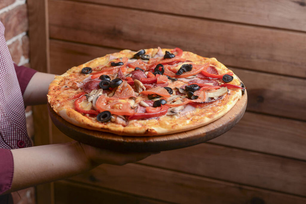 Delicious pizza with different kinds of cheese, tomatoes, black olives. Waiter holds a plate of tasty food. - Photo, Image