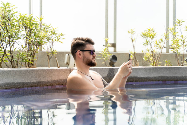 Jeune homme avec des lunettes de soleil utilisant son mobile dans une piscine intérieure
 - Photo, image