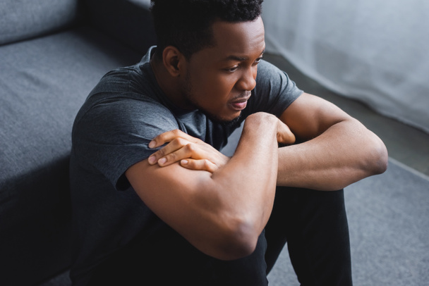 депресивний афроамериканський чоловік сидить на підлозі з схрещеними руками
 - Фото, зображення