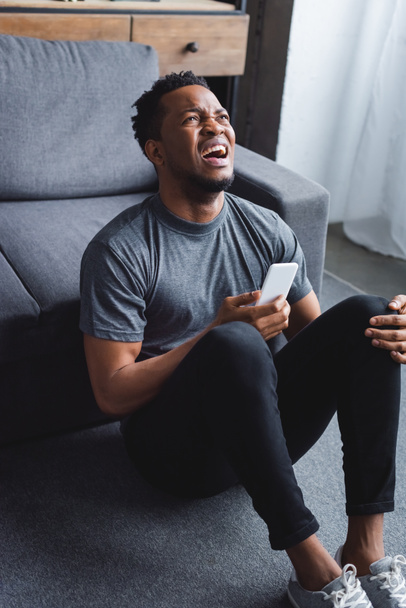 stressed african american man screaming and using smartphone at home - Photo, Image