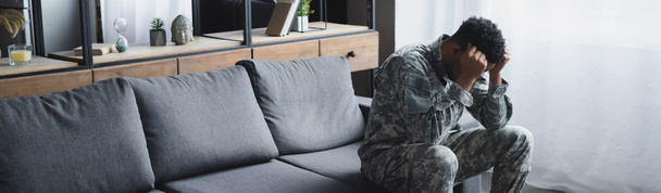 panoramiczne ujęcie smutnego afrykańskiego żołnierza w mundurze wojskowym cierpiącego na PTSD w domu - Zdjęcie, obraz