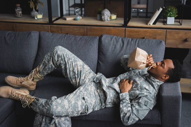 Afrikanischer amerikanischer Soldat in Militäruniform hält Papiertüte bei Panikattacke zu Hause - Foto, Bild