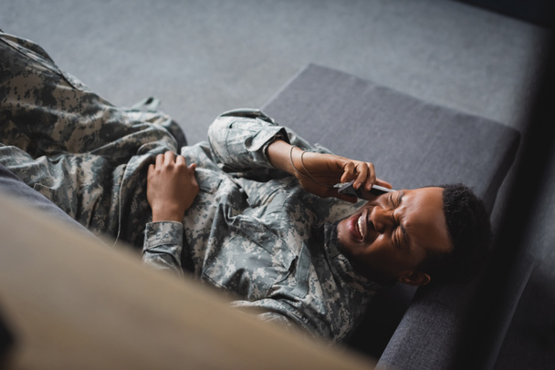 軍の制服を着たアフリカ系アメリカ人兵士が泣きながらスマートフォンで語り家でPTSDに苦しんでいるのを強調しました - 写真・画像
