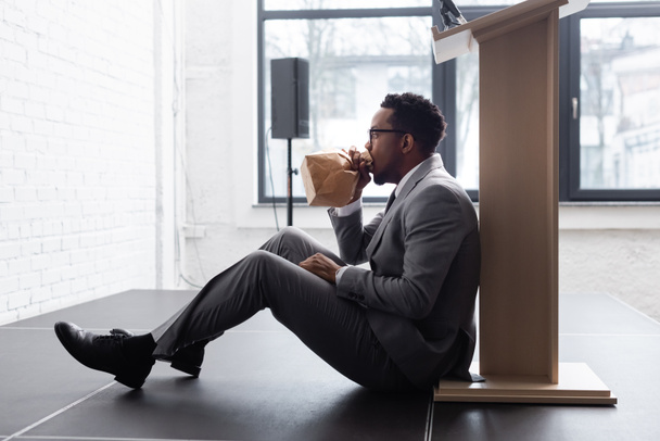 nervöser afrikanisch-amerikanischer Redner atmet mit Papiertüte und hat Panikattacke während Geschäftskonferenz im Büro  - Foto, Bild