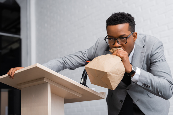stressed african american speaker breathing with paper bag and having panic attack on business conference  - Photo, Image