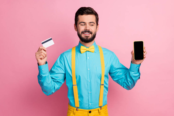 Portrait of his he nice attractive cheerful cheery confident bearded guy wearing mint blue shirt holding in hands cell bank card online pay app isolated over pastel pink color background - Zdjęcie, obraz