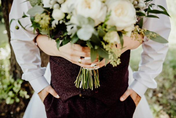 la novia abraza al novio y sostiene en sus manos un ramo de boda sobre un fondo borroso con una profundidad de campo poco profunda
 - Foto, Imagen
