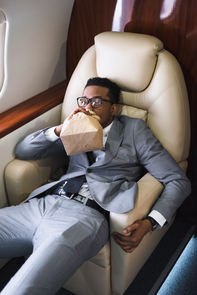 stressé homme d'affaires afro-américain respirant avec un sac en papier tout en ayant une attaque de panique pendant le vol en avion privé
 - Photo, image