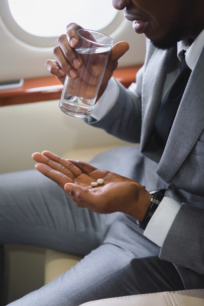 visão cortada do nervoso empresário afro-americano que toma pílulas enquanto tem ataque de pânico durante voo em avião privado
 - Foto, Imagem