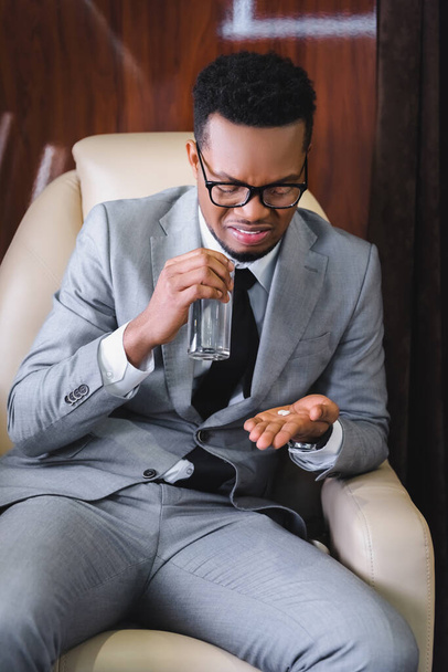 нервовий афроамериканський бізнесмен приймає таблетки під час нудоти або панічної атаки під час польоту на приватному літаку
 - Фото, зображення