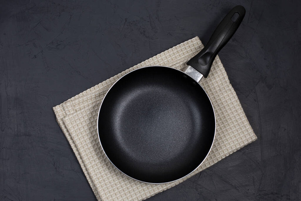 Empty black frying pan with kitchen towel on black table. Top view. Copy space. - Fotó, kép