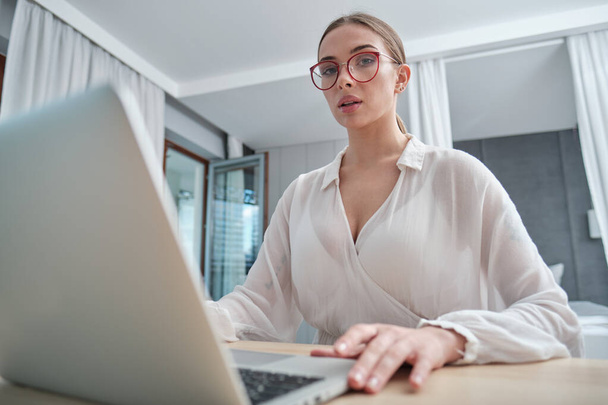 woman in eyeglasses sitting with computer on couch, looking outside, cannot concentrate on work, need some rest, feeling bored, need additional motivation, working remotely at home. - Photo, image