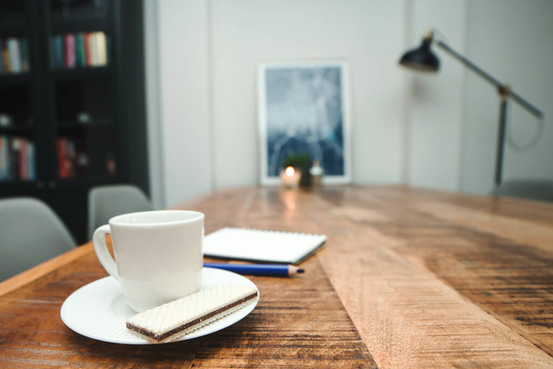 Luxury interior home with coffee cup on wooden table. White coffee cup and notebook. Morning planning. Modern apartment interior. Morning coffee mug. Business plan. Scandinavian style. - Photo, Image