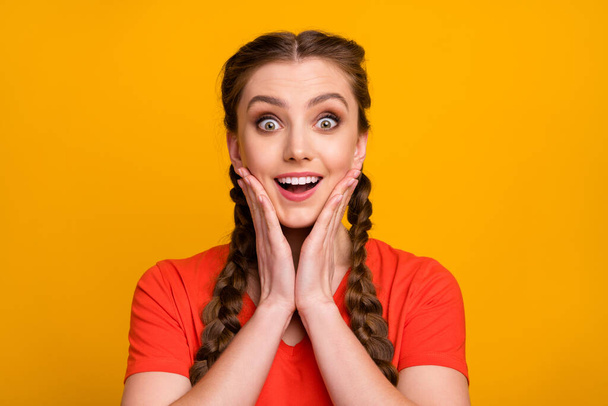 Closeup photo of attractive shocked funny lady two long braids open mouth listen unexpected good news arms on cheeks wear casual red t-shirt isolated vivid yellow color background - Fotó, kép